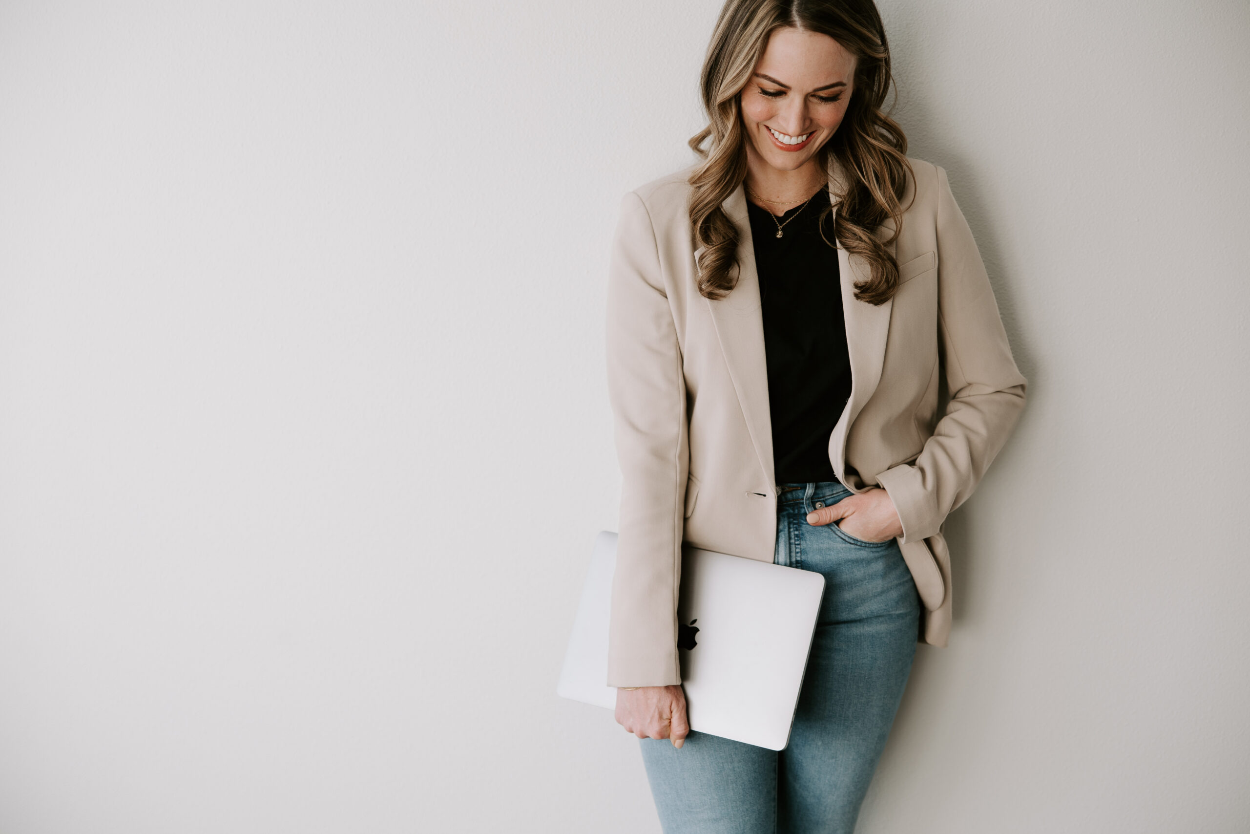 A website copywriter holding a laptop and leaning against a white wall