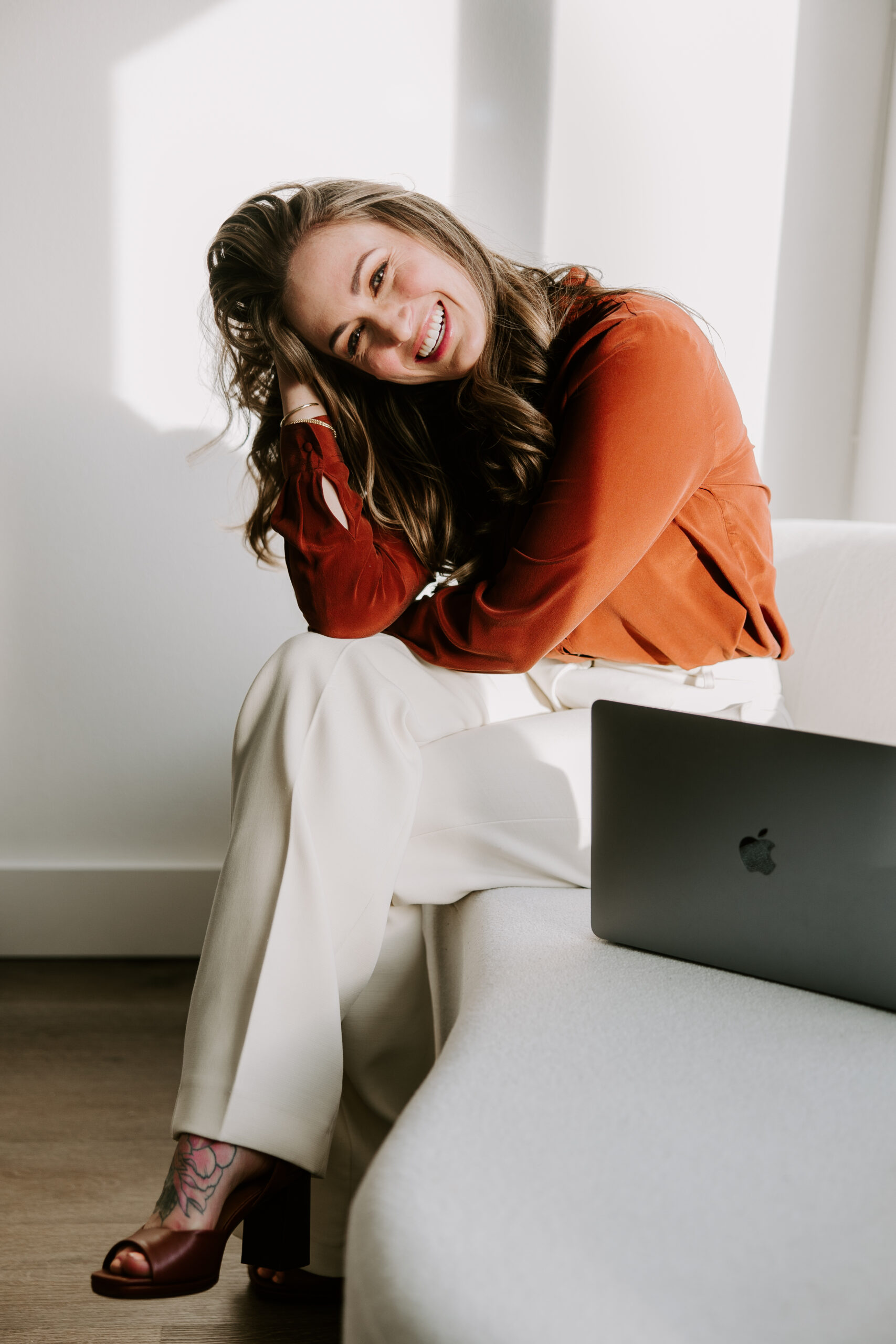 A website copywriter wearing an orange blouse sitting next to a laptop